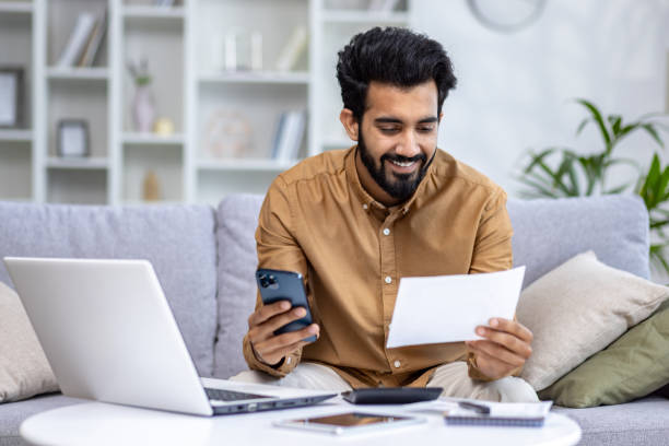 istock Smiling young man multitasking with smartphone and paperwork in cozy home office setting, productivity and comfort 2032813093