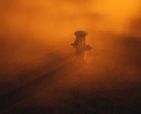 Fire hydrant supply on cracked tarmac street in mist at sunset.