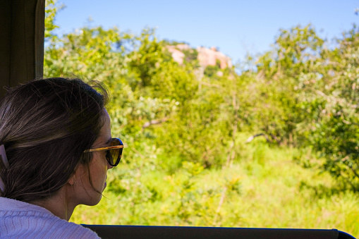 A woman is sitting on a 4wd seat, gazing out of the window at the passing scenery during the journey in a safari