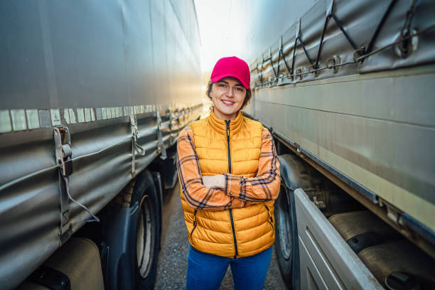 Portrait of a smiling female truck driver standing between truck vehicles. Transportation service