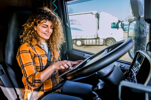 Cheerful female truck driver using a digital tablet in the cab of a truck