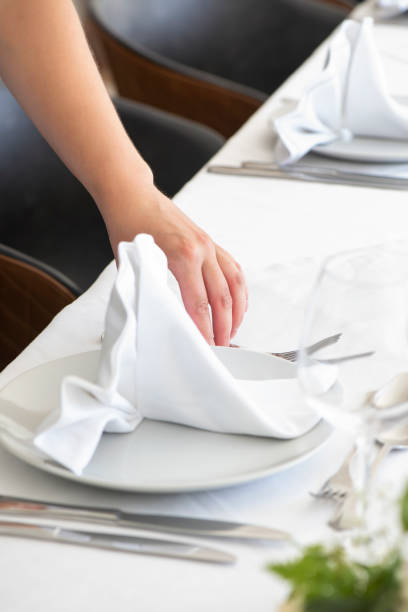 istock Woman's hand delicately folding a white cotton napkin, decorative technique adding an elegant touch to the table setup 2032893100