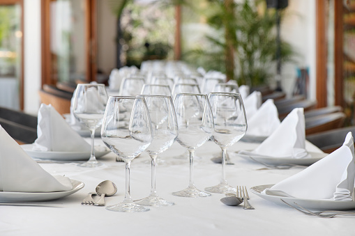 Table arrangement with polished cutlery on each side of elegant crookery, complemented by a cone-shaped cotton napkin, setup for a three-course meal symmetrically aligned with wine and water glasses.