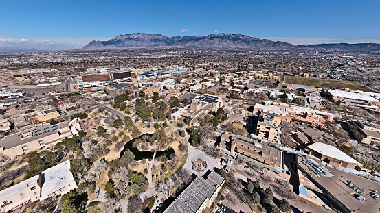 Wide panorama drone shot of UNM campus with duckpond, popejoy hall and the Sandia mountains