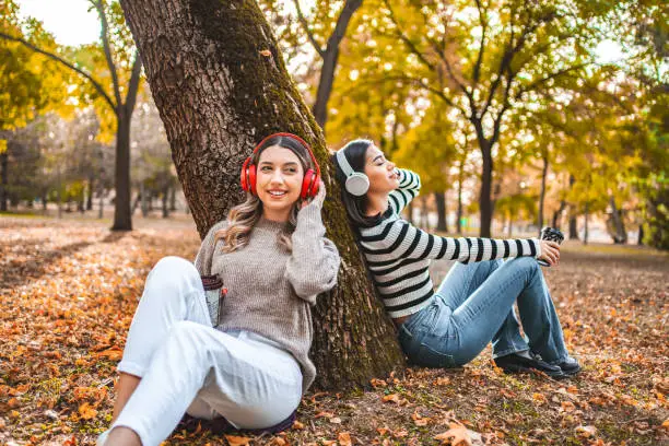 Two bestfriends listening to music in the park by the tree