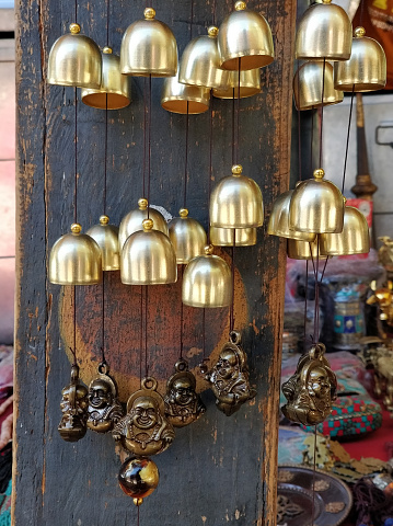 A variety of bells are suspended on strings from a weathered wooden door. The bells range in size and are made of different materials, creating a rustic and charming display.