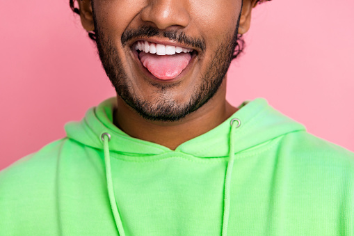 Close up cropped photo of funny young guy in green hoodie stick out protrude tongue childish behavior isolated on pink color background.