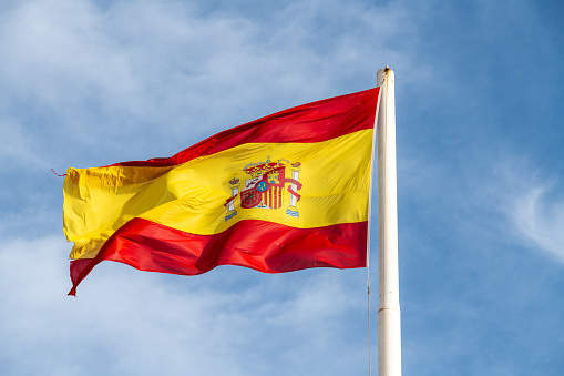 Cartagena, Murcia - Spain - 01-16-2024: Spanish flag flutters in the breeze, vibrant yellow and red with the national coat of arms, set against a clear blue sky