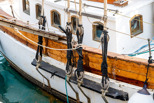 Old wooden sailing ship, closeup. Wooden steering wheel, ropes, rope ladder and bronze bell.