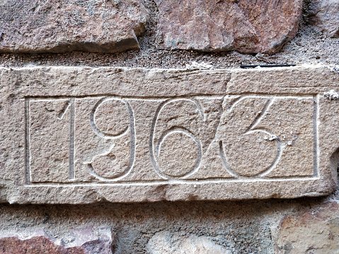 A detailed close-up view of a weathered brick wall, prominently displaying a painted number. The bricks show signs of aging and wear, adding character to the urban scene.