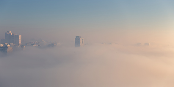 Morning fog over the city. Dense fog envelops the residential area. Buildings sticking out of the fog. Wide panorama.