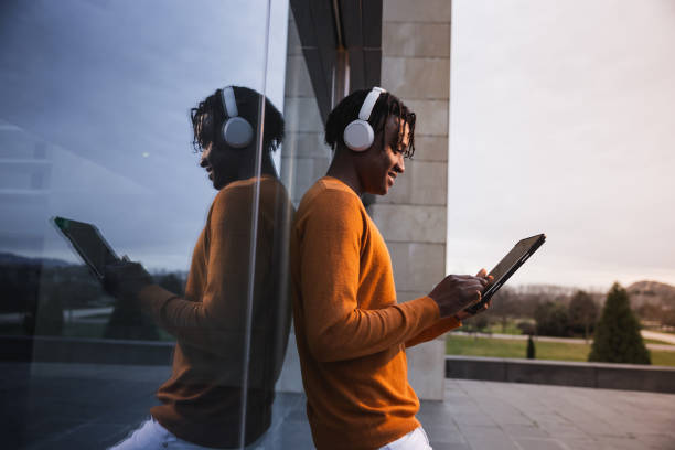 Young African American man reflected and engages with a tablet, immersed in the digital world amidst the architectural elegance of a cityscape.