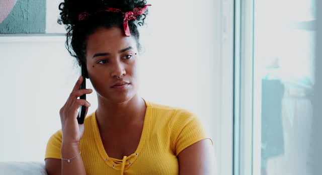 Young African American woman putting cellphone on the ear making a call at home seated on home couch. One candid black latina 20s girl calling someone