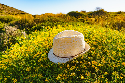 Summer hat on yellow flowers, mediterranean sea coast landscape in Spain. Hiking, camping, active lifestyle.