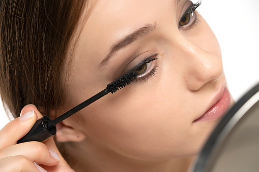 Portrait of a young woman applying mascara with brush on a white studio background