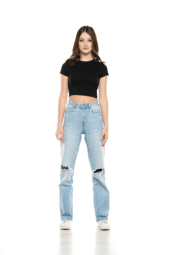 Young female model wearing ripped jeans and black shirt posing on a white studio background. Front view