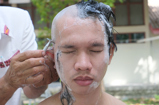 Portrait of a good-looking Thai man shaving his hair in order to become a monk.