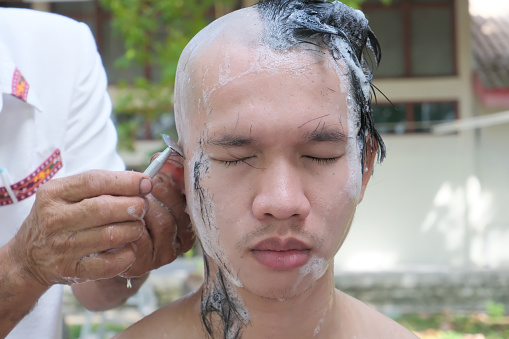 Portrait of a man about to become a monk undergoing a meticulous hair shaving ceremony.