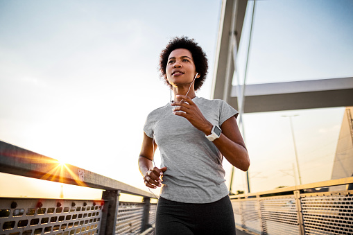Young African American woman exercising on the bridge at sunset