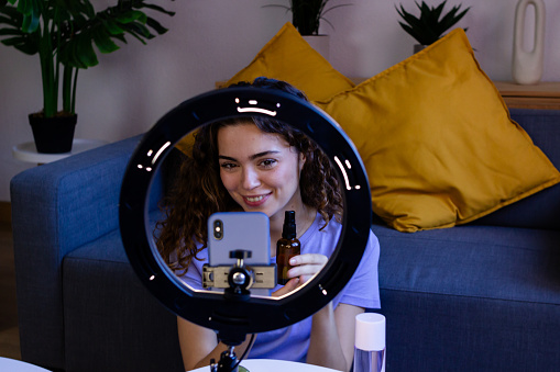 Cheerful woman recording a beauty blog using a smartphone and ring light.