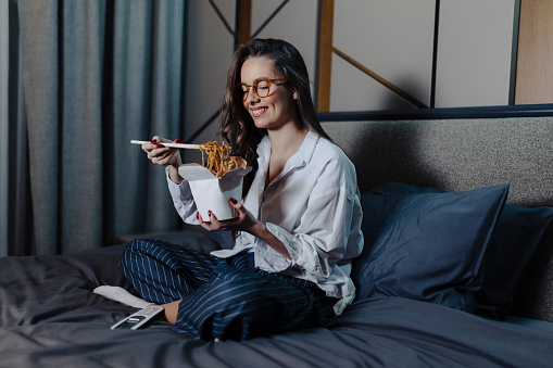 Woman eating pasta and watching movie at bed at night