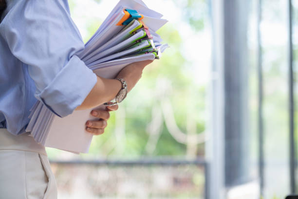 a young secretary is searching through the pile of documents on her desk to prepare for an executive meeting. the secretary looked exhausted from searching through the pile of documents on her desk. - mafia organized crime female women - fotografias e filmes do acervo