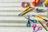 Overhead view of work tools used for crafts. Scissors, measuring tape, pencil, adhesive tape, penknife