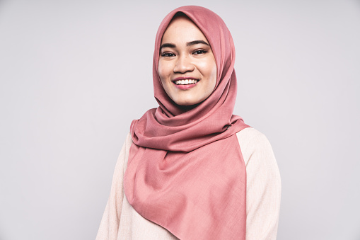 Happy smiling Malaysian Woman standing in Studio, looking towards the camera with a bright happy natural smile. Young woman wearing a fashionable modern Hijab - Headscarf. White Background Portrait Studio Shot. Kuala Lumpur, Malaysia.
