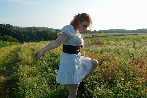 A pretty young woman wearing white short dress, running in a meadow in green nature