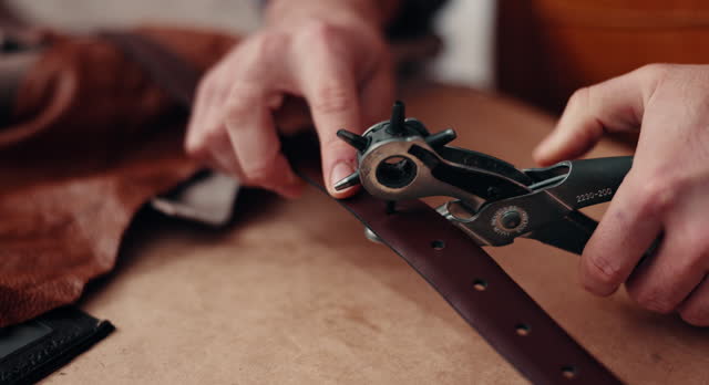 Hands, leather factory and hole punch for belt, fabric or industry for manufacturing at desk in closeup. Entrepreneur, storage check or designer for creativity, fashion or cloth for quality assurance