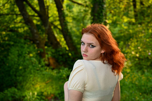 Portrait of a young redhead  girl in green nature, looking seriously at the camera