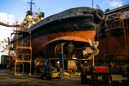 Commercial shipping tanker undergoing refurbishment, extensive renewal of hull and propulsion system, showcasing heavy industry, maritime commerce and specialized labor at shipyard facility.