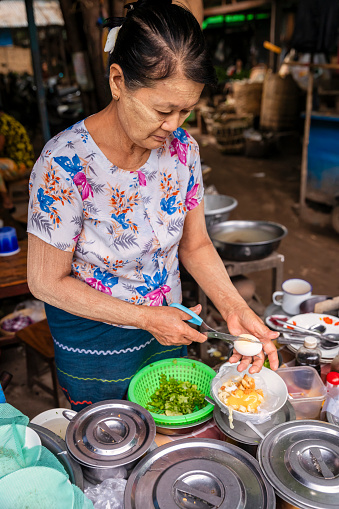 Burmese woman serving breakfast on a local market in Bagan, Myanmar. It is quite popular in Myanmar to use scissors to cut eggs or vegetables.