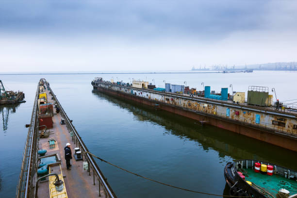 istock Vessel maneuvers into floating dock at maritime yard for repairs, cloudy skies, surrounded by port infrastructure amidst calm waters. Specialist crew prepare for docking, maritime operations. 2033398548