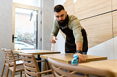 Shot of a mid adult male waiter cleaning the tables while working in a restaurant