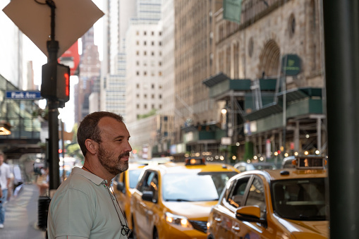 A man stands in profile against the backdrop of yellow cabs and bustling city streets.