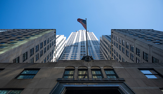 Looking up between towering skyscrapers, an American flag flies against the blue sky.