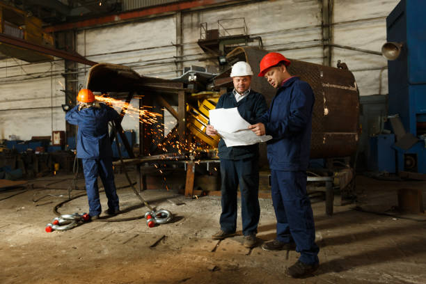 istock Engineer and worker consult over heavy machinery production, reviewing industrial grapple design in factory. Team analyzes project specs, steel manufacturing issues in workshop, safety helmets worn. 2033408710