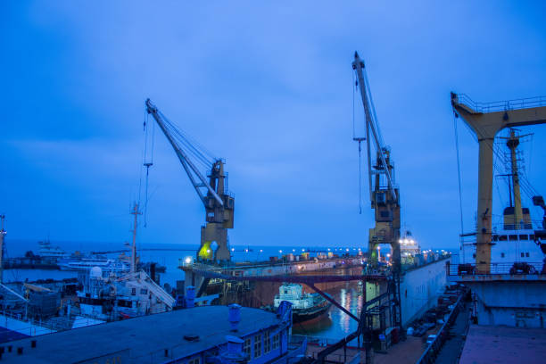 Twilight at shipyard with floating dock, vessels undergoing repair amid towering cranes. Maritime industry, heavy machinery at work, shipping business infrastructure, nautical vessel maintenance. Maritime industry, heavy machinery at work, shipping business infrastructure, nautical vessel maintenance. Twilight at shipyard with floating dock, vessels undergoing repair amid towering cranes. merchants gate stock pictures, royalty-free photos & images