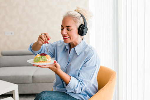 Beautiful woman eating dessert while wearing headphones and listening music at home