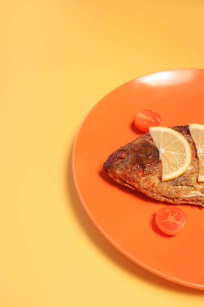 serving a dish with fish decorated with lemon slices and cherry tomatoes on an orange plate.