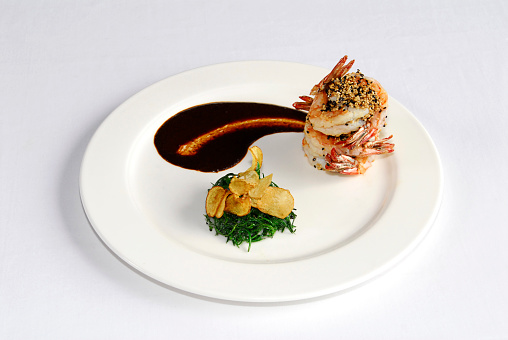 plate of sesame covered shrimp with Mexican mole sauce, French fries and spinach on a white tablecloth in a restaurant