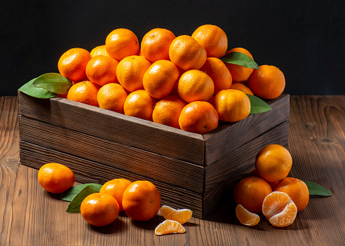 Group of tangerines with green leaves in a wooden box on a dark background