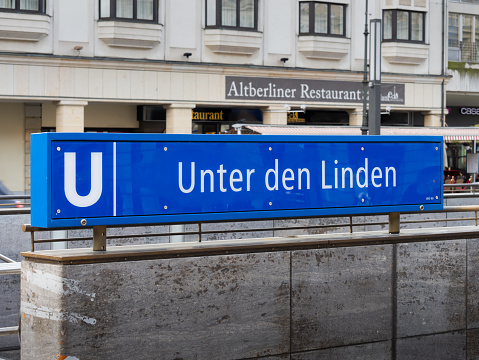 Berlin, Unter den Linden U-Bahn station sign next to the building entrance. Blue guidance with the location name. Public transportation service in the capital city.