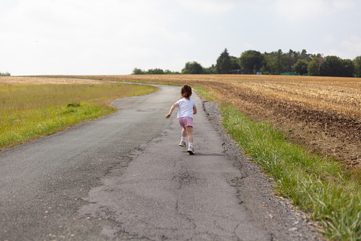 Little girl running on a country road in the middle of the field