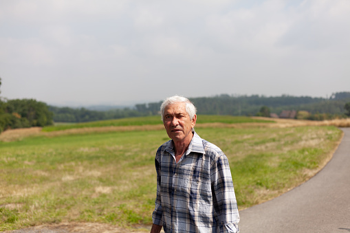 Portrait of an elderly man standing on the road in the countryside