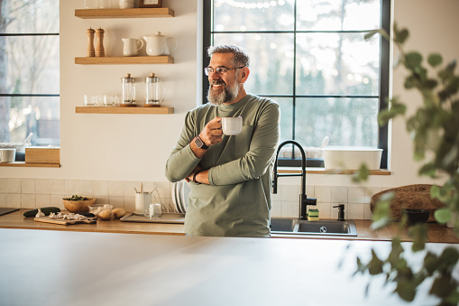 Mature man standing alone in kitchen, drinking coffee and enjoying in his morning routine.