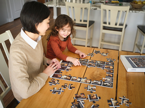 A four year old girl with her mother, doing a jigsaw puzzle together in their home.