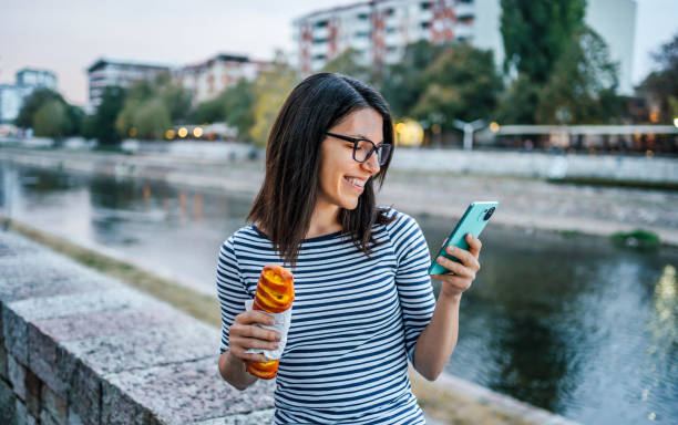 istock Woman eating pastry and using smartphone on the quayside 2033690879
