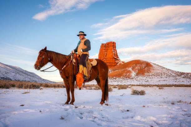 A ranch worker on a horse poses for a portrait at a Wyoming horse ranch in the winter in a rural landscape.